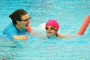 A female swim instructor cheers on a young child swimming in a pool