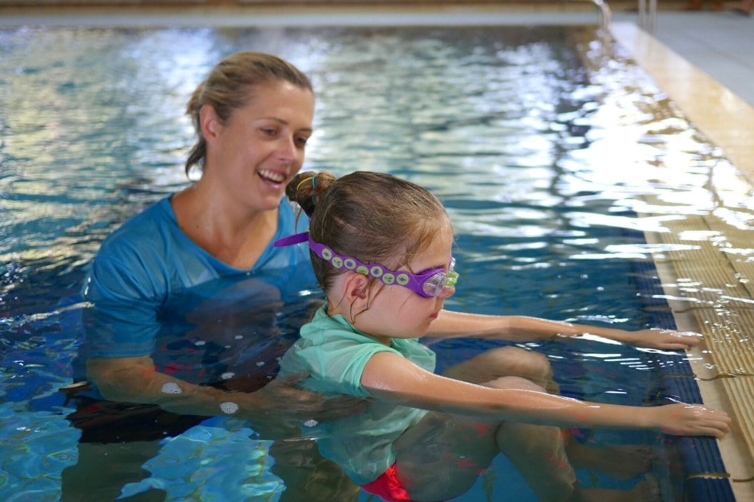 A female aquatic therapistr is teaching a young girl in a swimming pool.