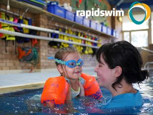 Female swimming teacher working with a young girl in a swimming pool during a lesson.