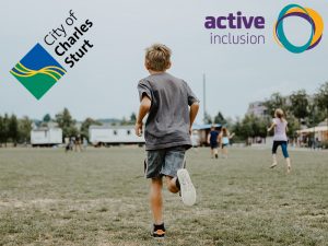 Image of a young boy running across grass in a outdoor park area away from camera. In the background other children are also running. The City of Charles Sturt and Active Inclusion logos appear at the top of the image