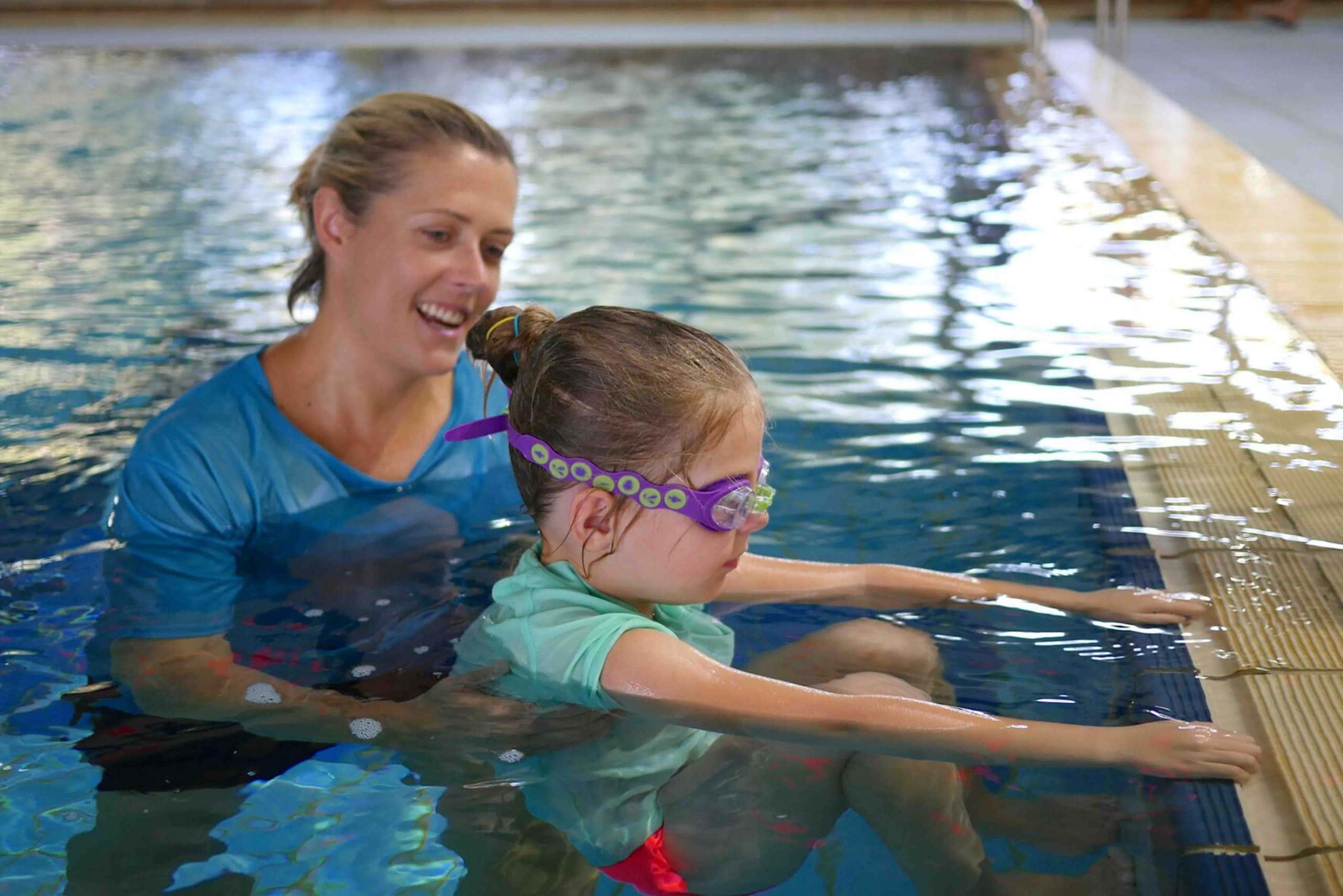 A female swimming instructor is teaching a young girl in a swimming pool.