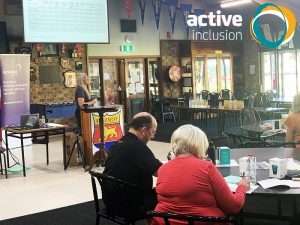 Image shows Active Inclusion General Manager Katrina Ranford at a podium in a sport club rooms talking to a group of people sitting at tables. The Active Inclusion logo appears in the top right hand corner.