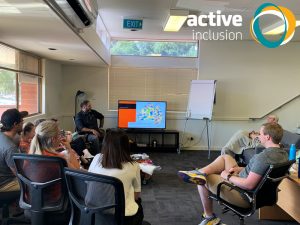 Image of office staff listening as Haydyn from Bookabee presents session on Aboriginal Cultural Sensitivity and Respect Training. The Active Inclusion logo appears in the top right hand corner.