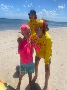 A Seabirds Nippers program participant laughing with their program buddy who is dressed in Surf Life Saving uniform and has their arm around their shoulders.
