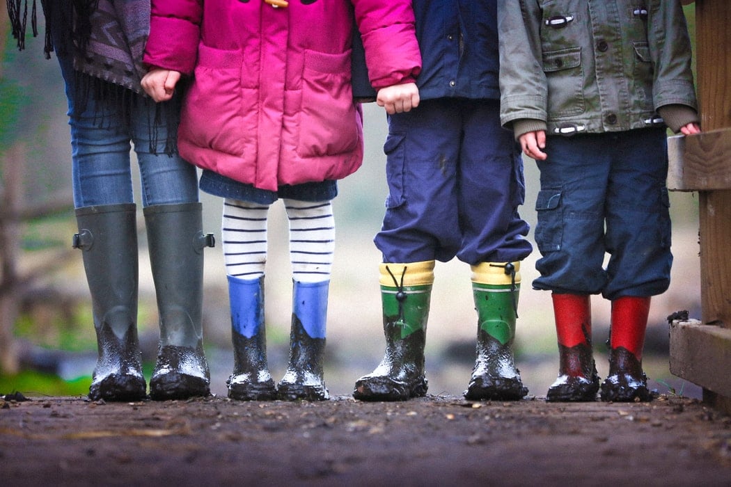 A group of 4 children stand on a path outside in a row holding hands